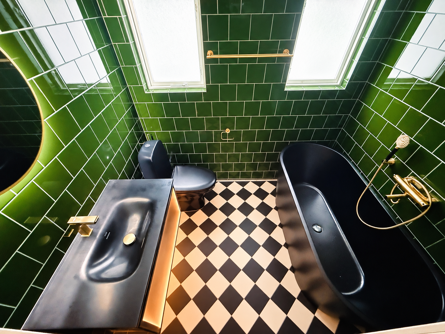 Renoverat badrum med grönt kakel, svart badkar, svart handfat och mässingsdetaljer.