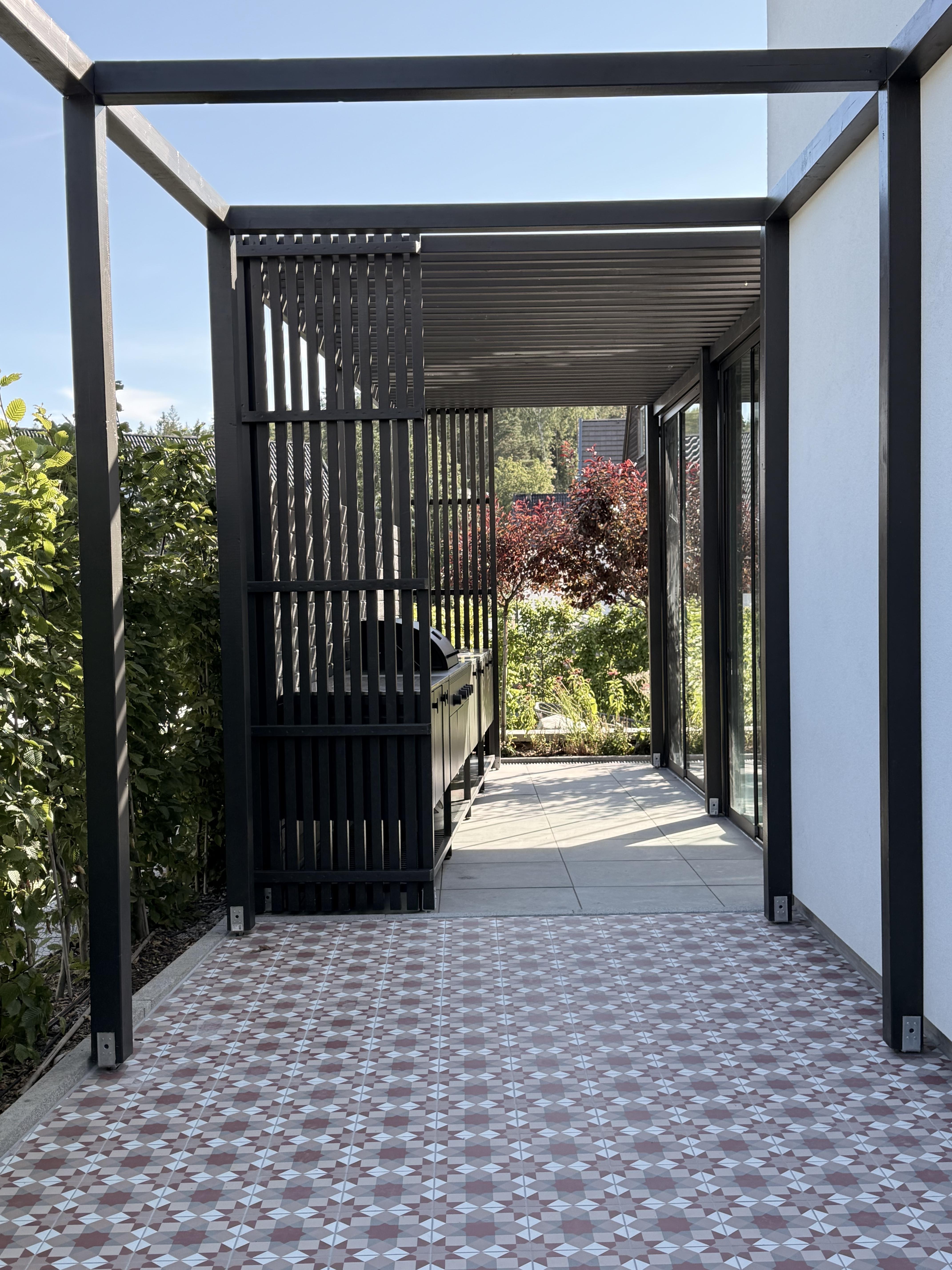 Svartmålad platsbyggd träpergola med ribbtak och insynsskydd intill en inglasad PERGOLUX pergola i Stockholm.